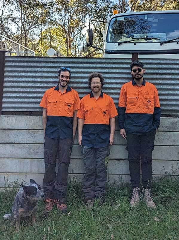 The team of qualified arborists at Heartwood Tree Care wearing hi-vis protective shirts, standing in front of the chipper truck.